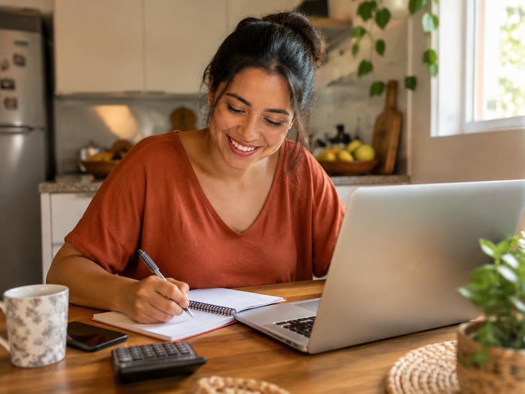 Pessoa organizando as finanças em casa com caderno e notebook